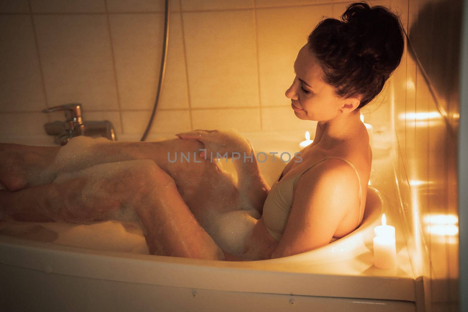 A woman is sitting in a bathtub with candles lit around her. Scene is relaxing and calming