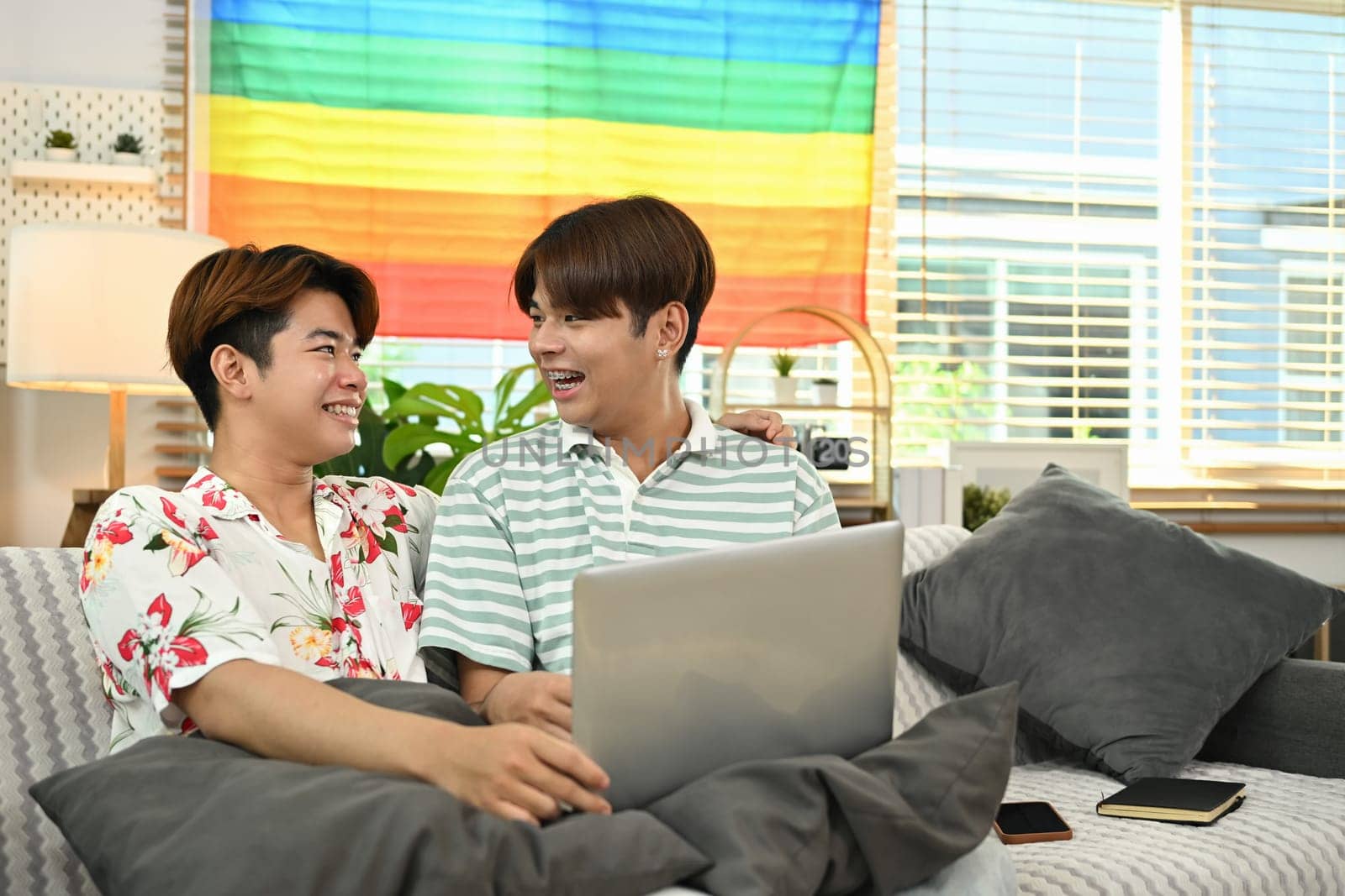 Young gay couple sitting on couch and surfing the net together at home. LGBTQ people lifestyle concept.
