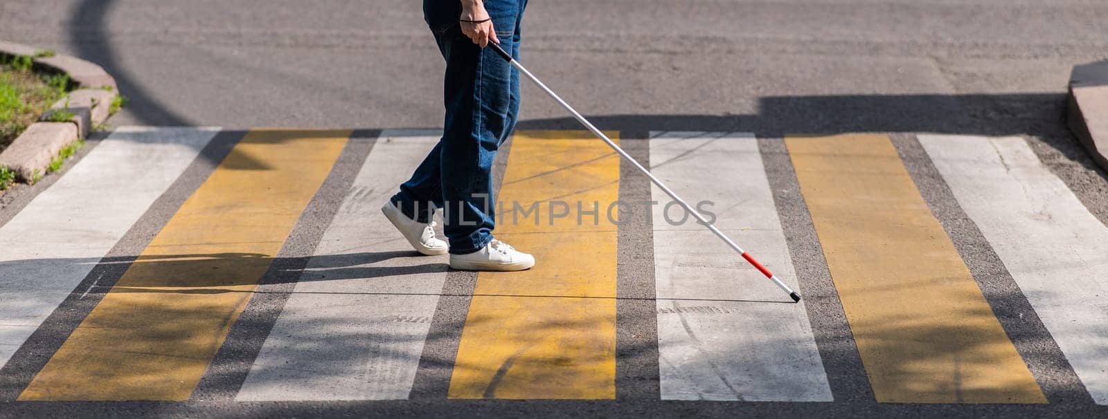 Close-up of the legs of a blind woman crossing the road at a crosswalk with a cane. by mrwed54