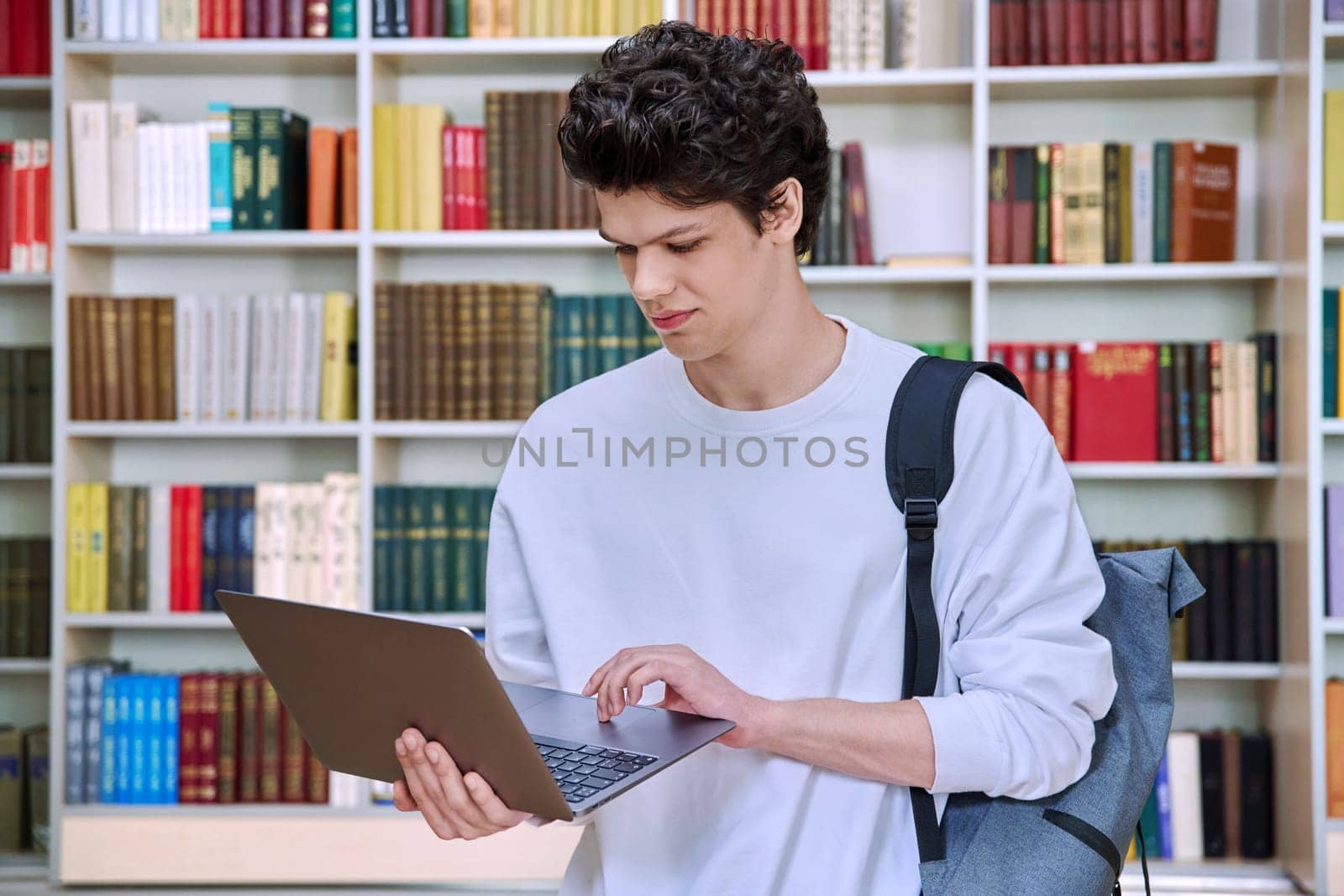 Portrait of handsome serious confident smart young male student with laptop computer in educational building in library. Education internet technology e-learning, learning services applications, youth