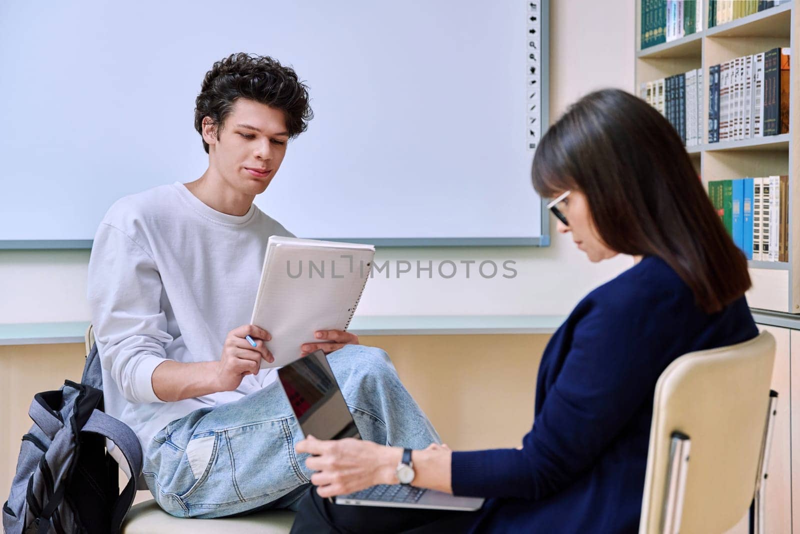 Guy college student talking studying with female teacher. Mentor and student together in the classroom. Education, training, mentoring, teaching, youth concept