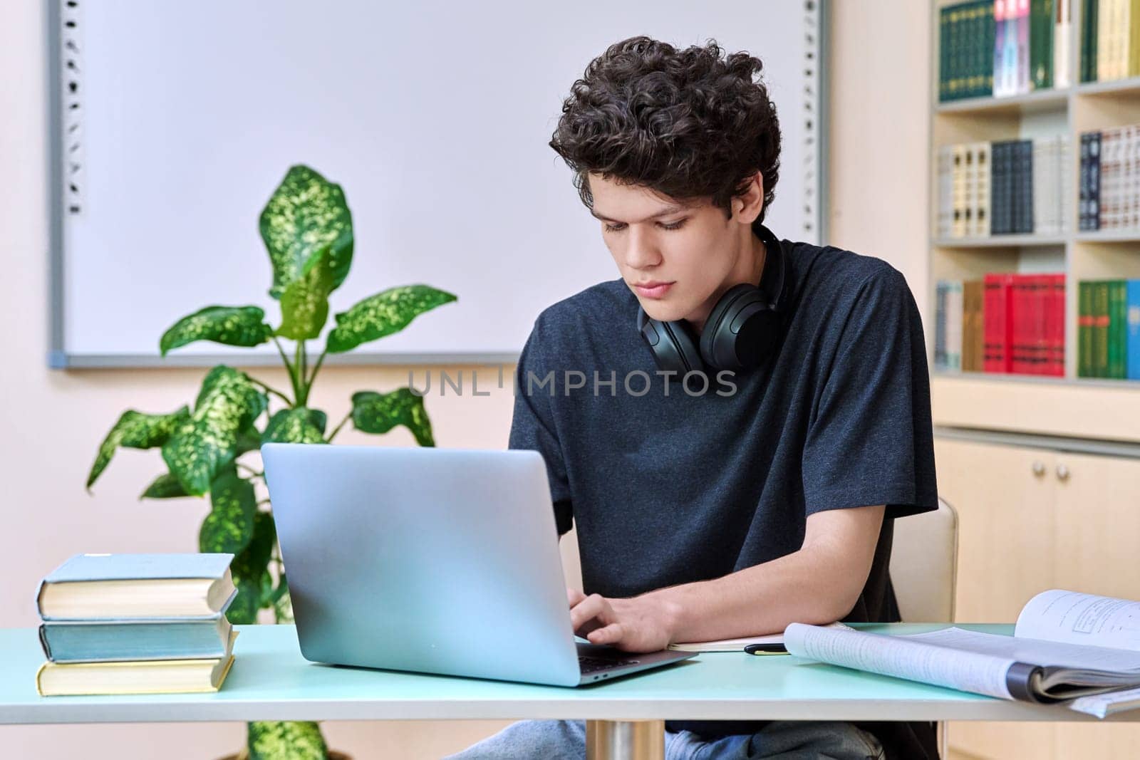 Portrait of college student guy sitting at desk with laptop computer and textbooks inside educational library classroom. Education internet technology e-learning learning services applications youth