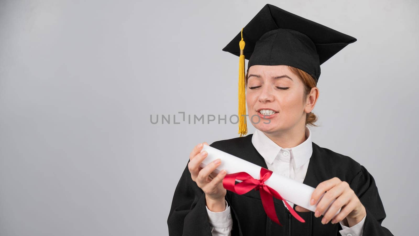 Smiling woman in graduation gown holding diploma on white background