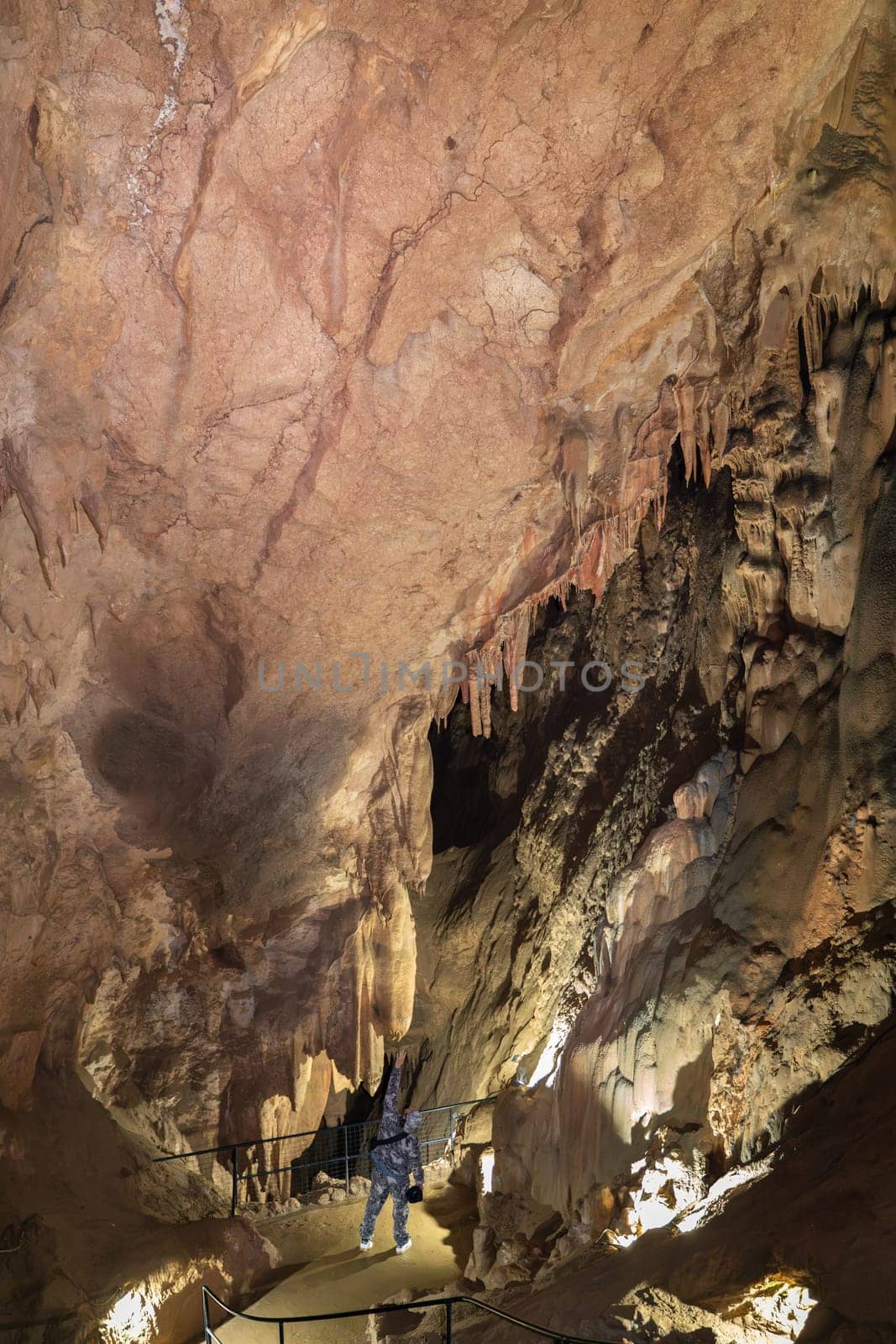 A man is walking through a cave with a large rock ceiling. The cave is dark and the man is holding a flashlight