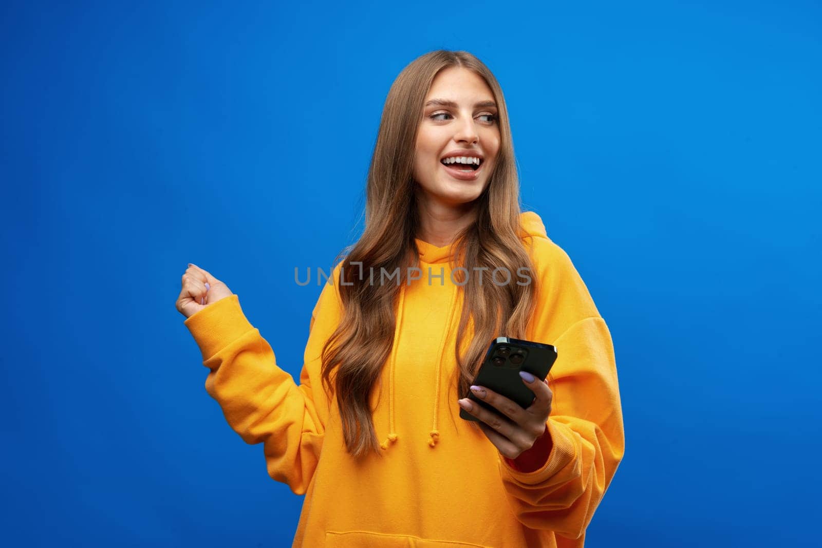 Portrait of young beautiful woman texting on the phone against blue background in studio