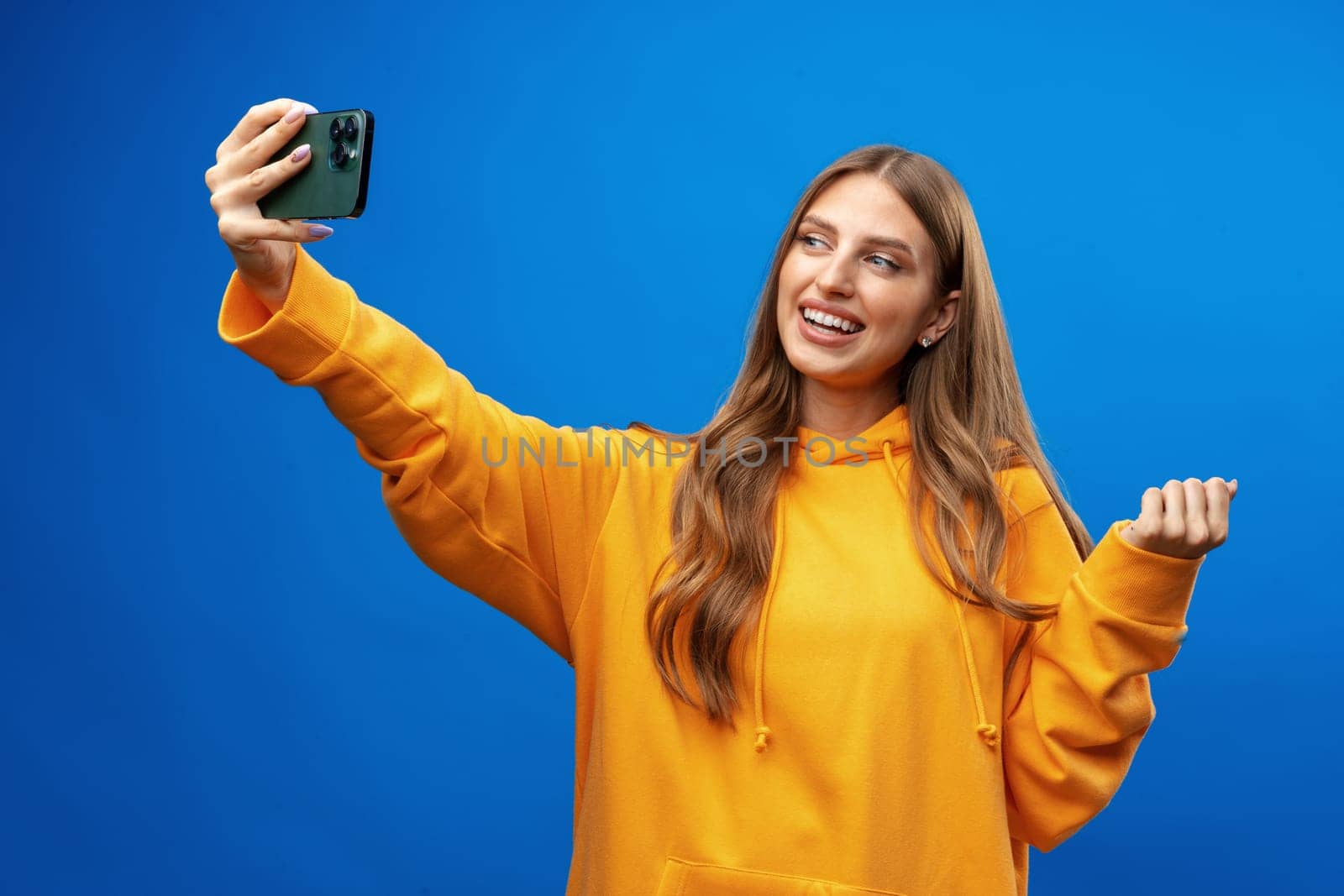 Photo of attractive young woman takes selfie photo on smartphone on blue background in studio