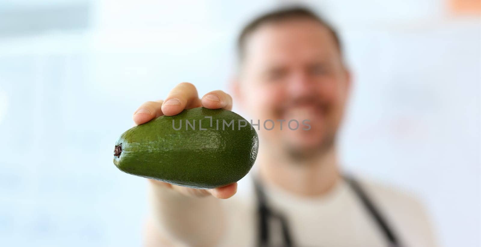 Chef Showing Exotic Green Avocado Photography. Man Holding Ripe Tropical Fruit in Hand. Delicious and Organic Vegetarian Kitchen. Fresh and Healthy Food for Vegan. Fresh Ingredient Partial View Shot