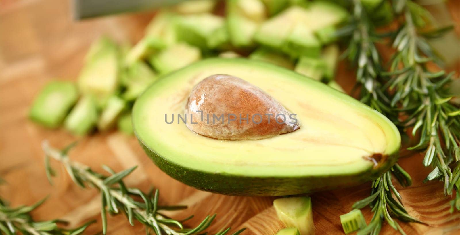 Tropical Avocado Fruit Half Holding Brown Seed. Exotic Ingredient on Wooden Cutting Board. Dieting and Healthy Food with Rosemary Herb. Tasty Appetizer. Partial View Horizontal Photography