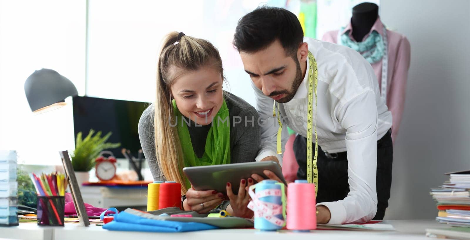 Sewing Needlework Technology Tailoring Concept. Two Professional Designers Looking in Digital Tablet in Handycraft Fashion Design Workshop. Creative Team Meeting. Couple Work on Trendy Clothes