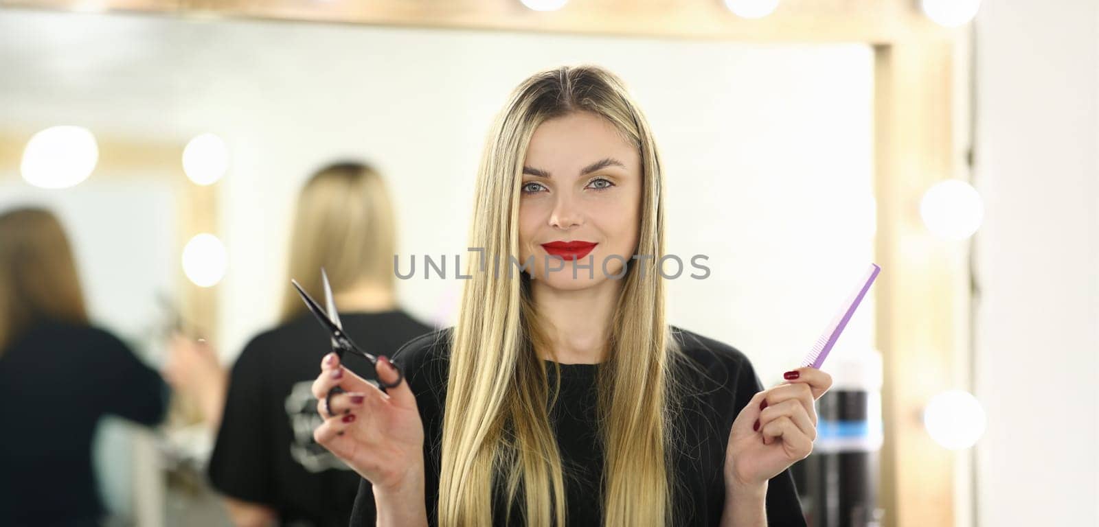 Hairdresser Woman Holding Scissors and Hairbrush. Blonde Hairstylist with Tool for Hair. Female Beautician with Comb for Hairdo Standing in Beauty Salon. Haircut Stylist Looking at Camera Shot