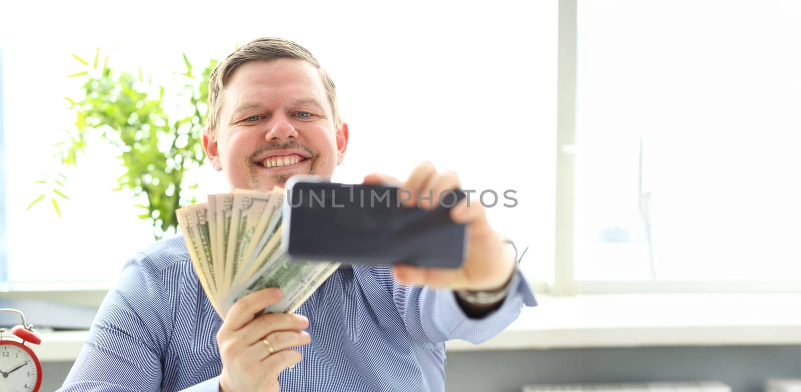 Man making self photo with mobile phone camera posing with pile of US money holding in hands