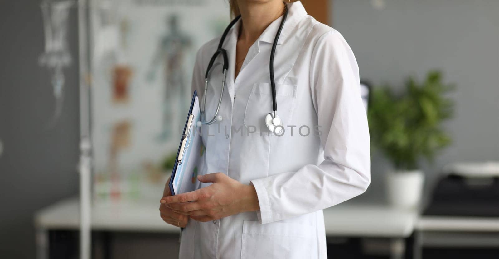 Woman standing in modern hospital office and wearing white doctor robe with stethoscope to perform medical examination to ill patients. Health checkup concept