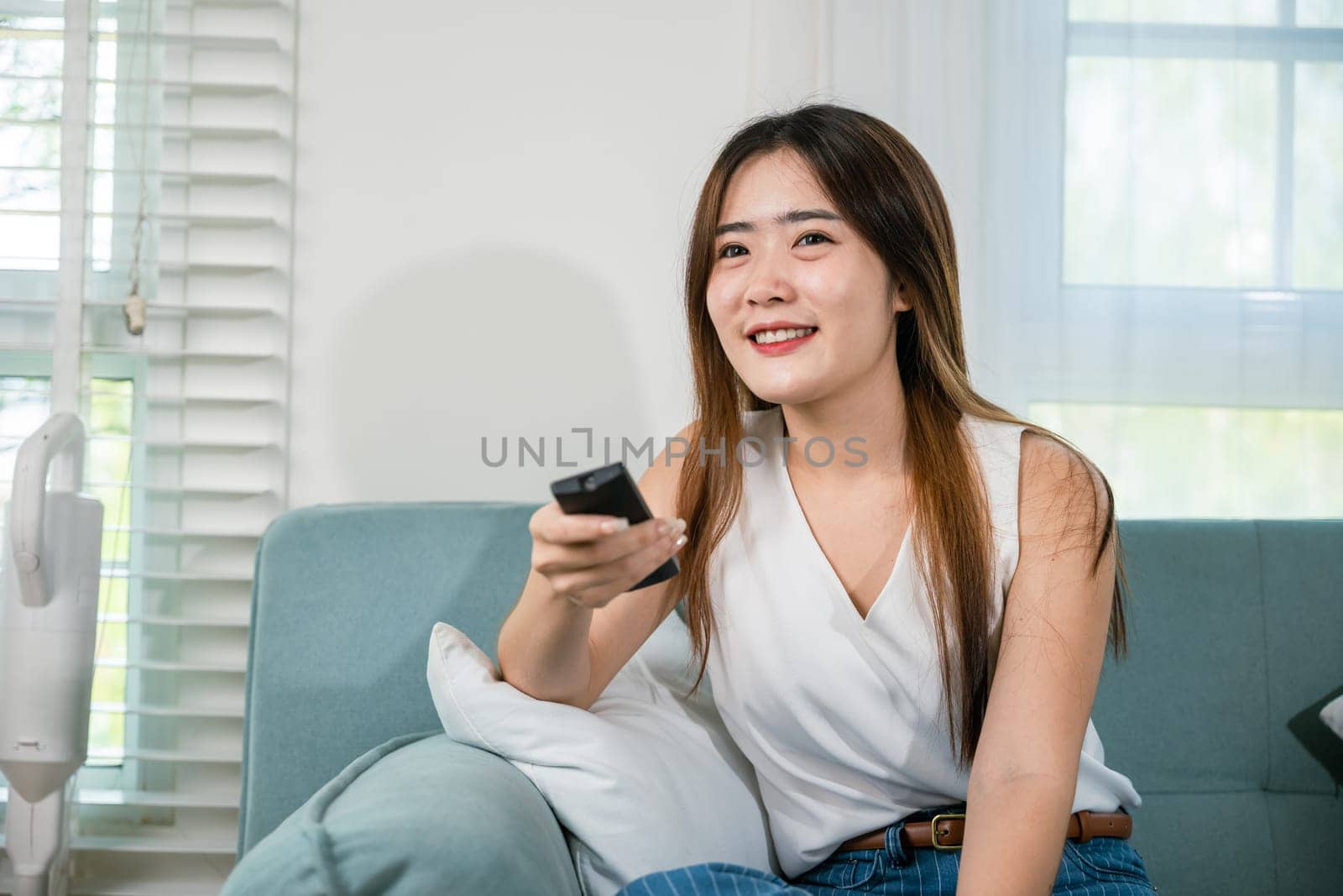 Asian young woman smiling sitting relax watch TV holding remote control on sofa in living room, Happy female fun movie holding remote watching television, Activity lifestyles concept