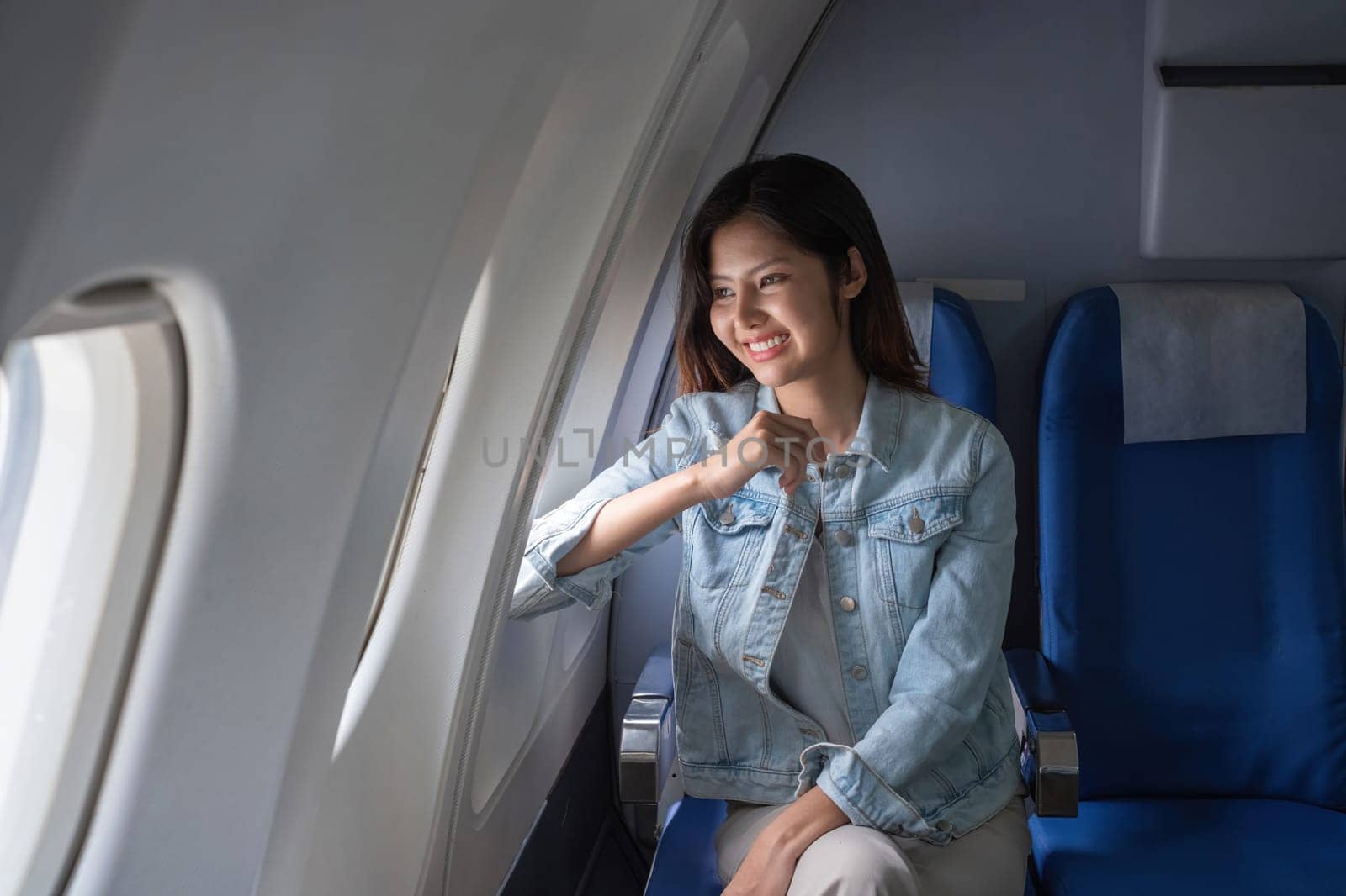 Asian woman smiling while sitting by airplane window. Concept of air travel, relaxation, and leisure.