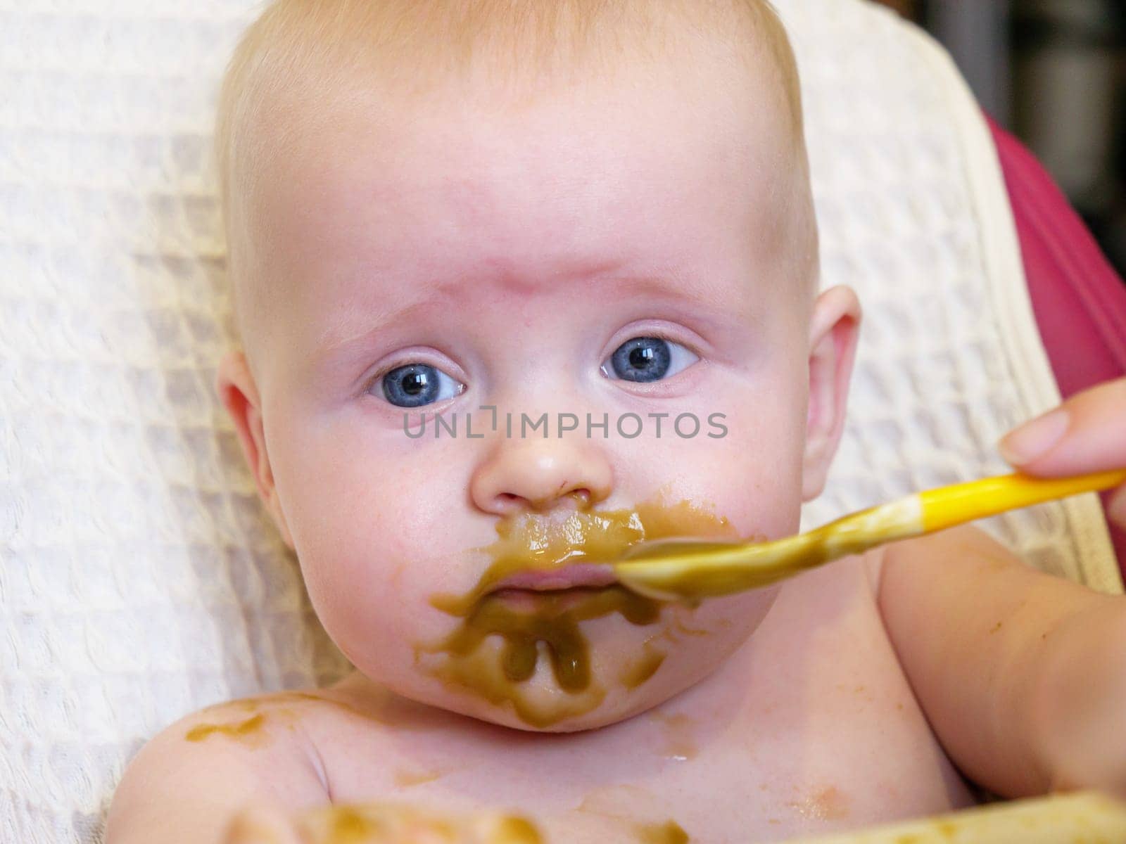 Mom feeding little boy with broccoli puree. Child at the age of six months eats broccoli while sitting on a baby chair.