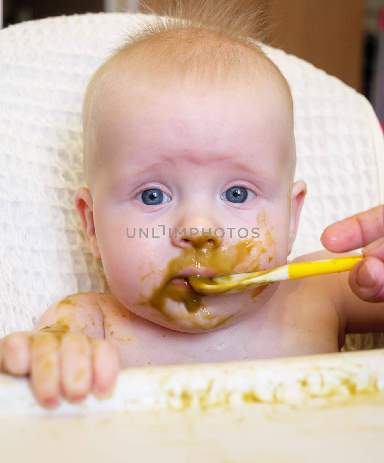 Mom feeding little boy with broccoli puree. Child at the age of six months eats broccoli while sitting on a baby chair.