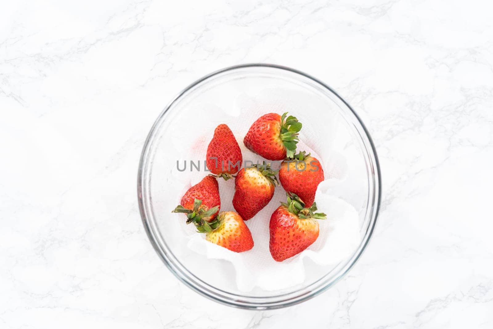 Freshly washed and dried strawberries are carefully arranged in a glass bowl lined with paper towel, ready for snacking or further use.