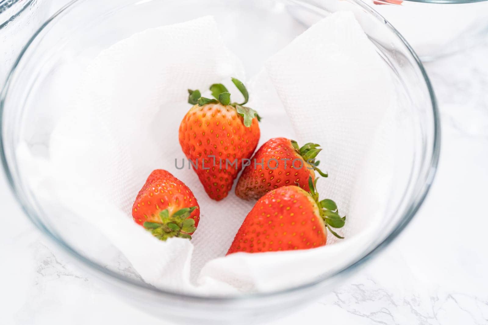 Freshly washed and dried strawberries are carefully arranged in a glass bowl lined with paper towel, ready for snacking or further use.