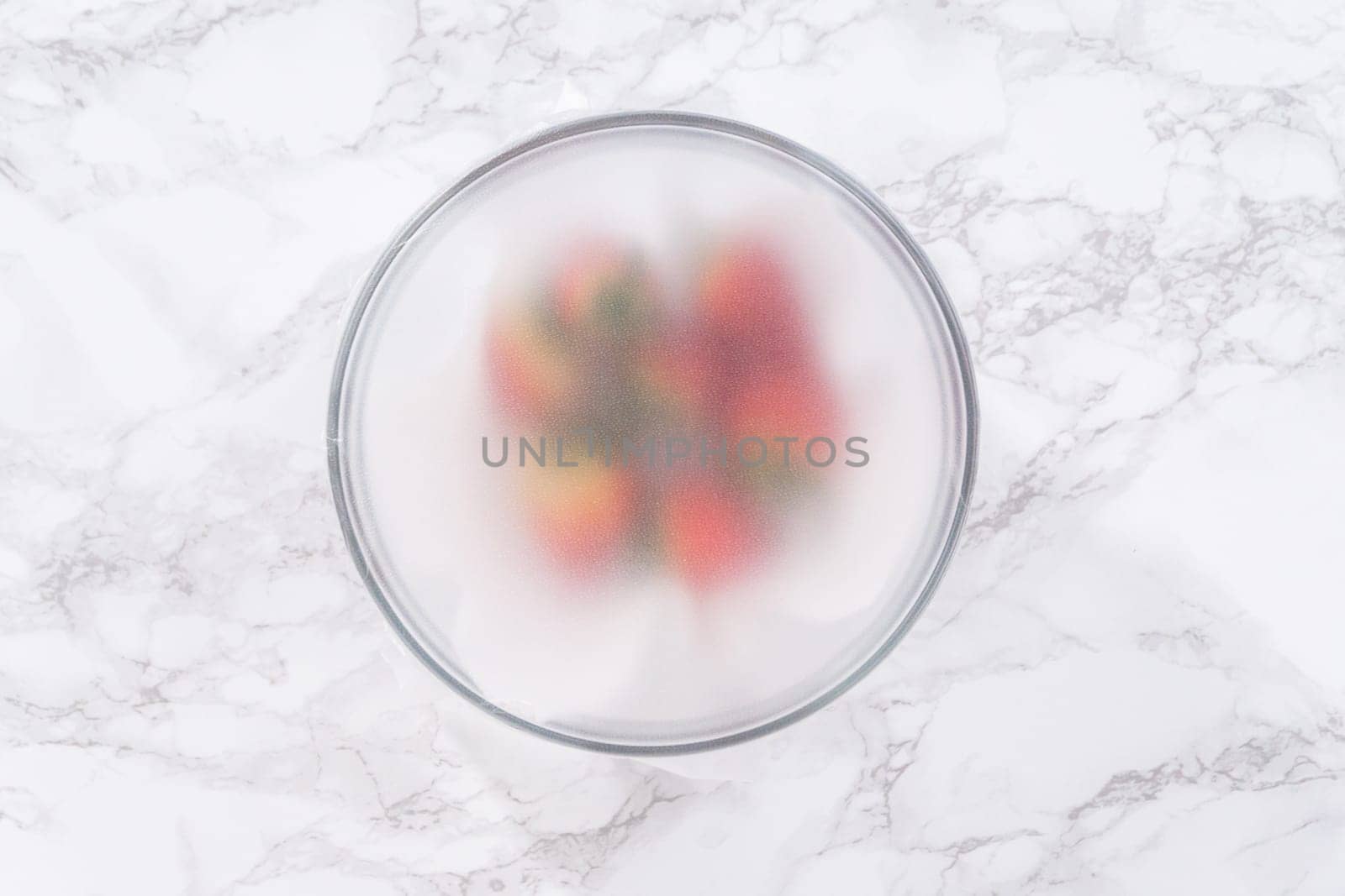 Strawberries, freshly washed and dried, are neatly stored in a glass bowl lined with a paper towel and securely covered with plastic wrap to maintain freshness.