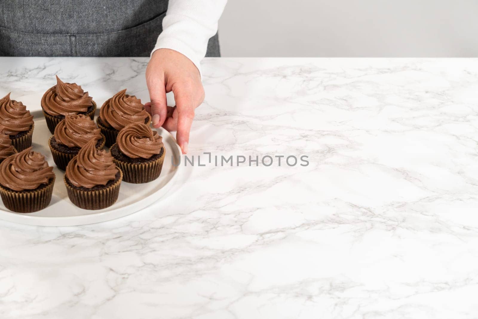 Freshly baked cupcakes have been masterfully infused with rich caramel and adorned with velvety chocolate frosting, all elegantly presented on a pristine white serving plate.