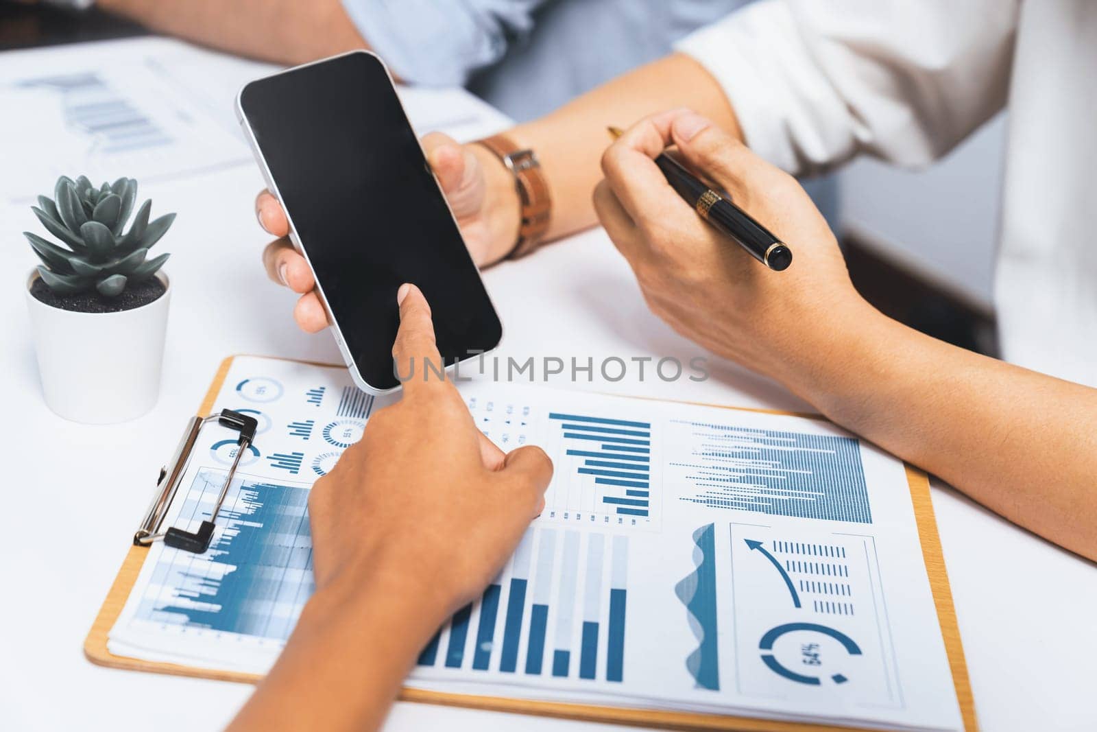 Diverse corporate audit team or company bookkeeper and accountant consultant calculate account expenses and income budget for tax refunds using blank screen smartphopne in busy workspace. Prudent