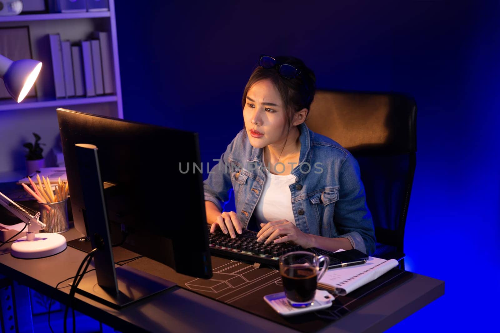 Stressful young beautiful asian creative looking on pc to search project creator social media online with planning channel strategy reach of more viewer home at neon modern office at night. Stratagem.