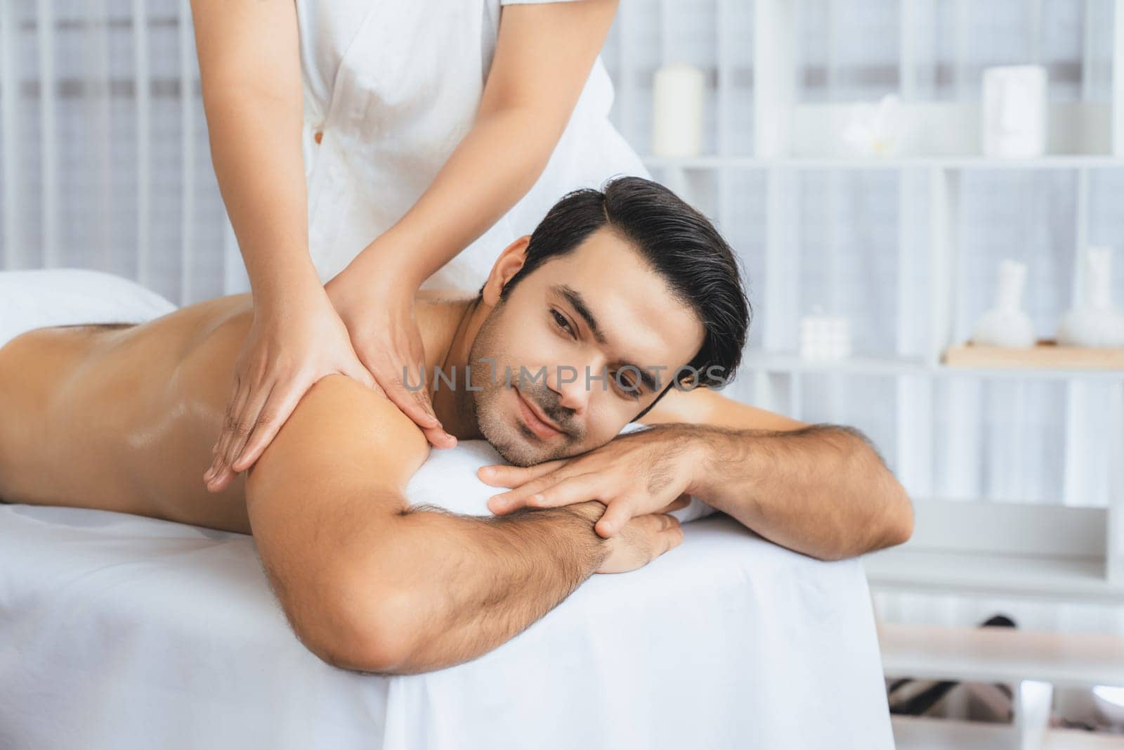 Caucasian man customer enjoying relaxing anti-stress spa massage and pampering with beauty skin recreation leisure in day light ambient salon spa at luxury resort or hotel. Quiescent