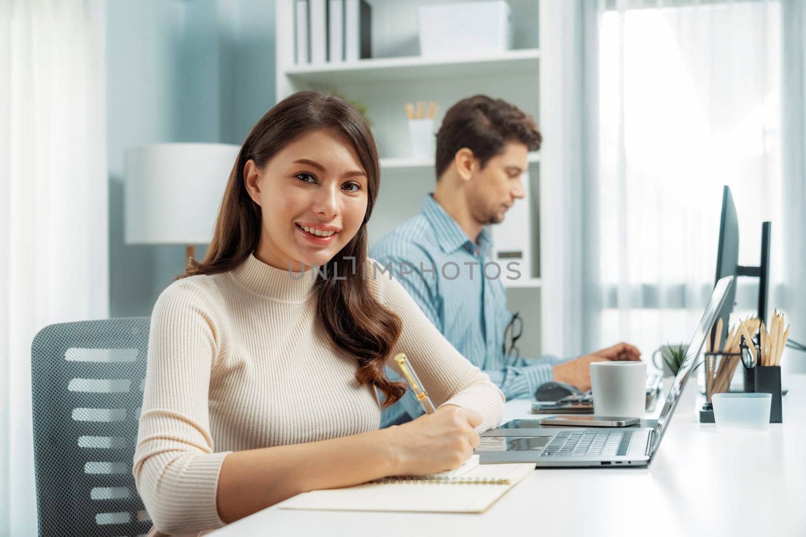 Smiling beautiful woman taking crucial note on paperwork, looking at camera photo shooting portrait business pose profile while working with smart coworker at modern office at morning time. Postulate.