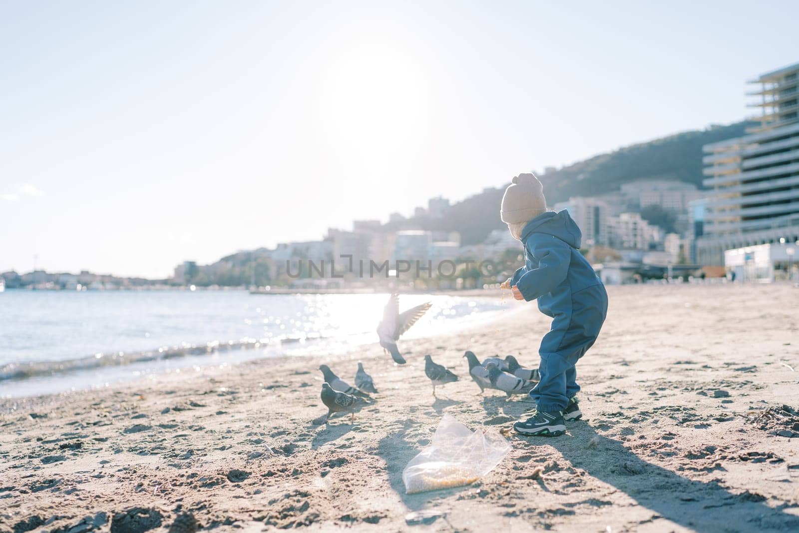 Little girl feeding pigeons on a sandy beach. High quality photo