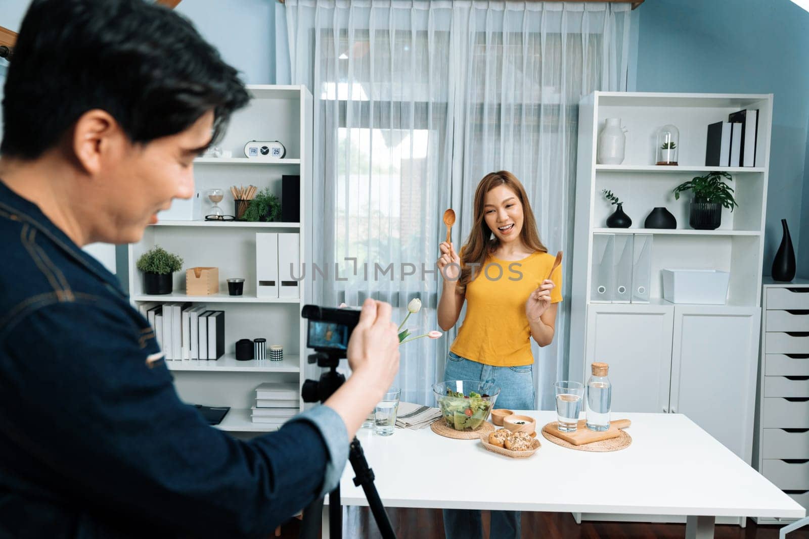 Asian beautiful woman food specialist blogger teaching how to mixed salad easy cooking in glass blow on live channel recorded by smart cameraman streaming lifestyle on social media concept. Infobahn.