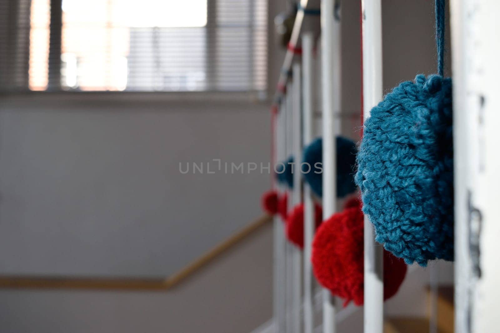 Close-up of colorful yarn pom-poms hanging on a staircase railing with a blurred background.