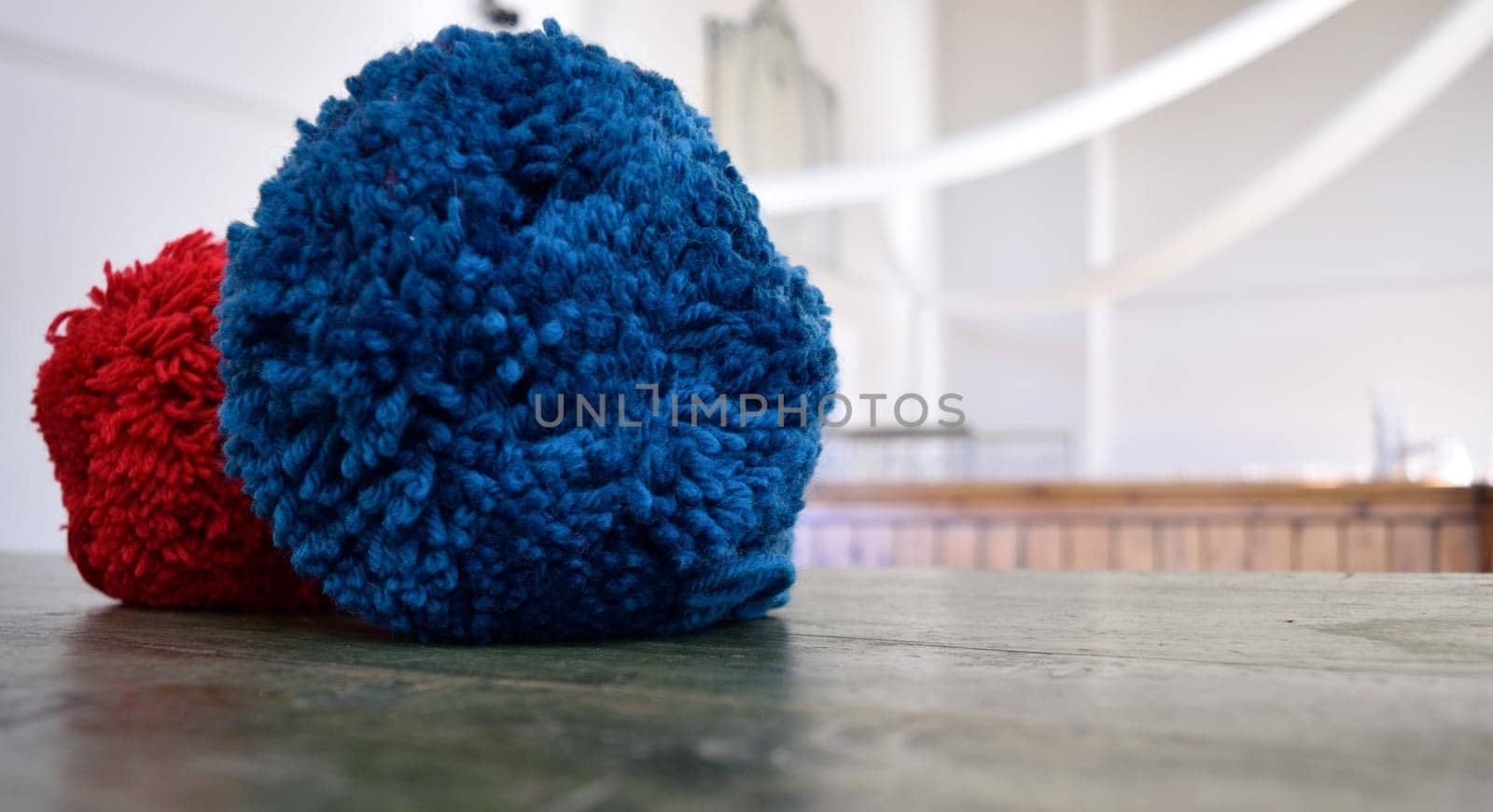 Close-up of a red and blue pom-pom on a wooden surface with a blurred background.