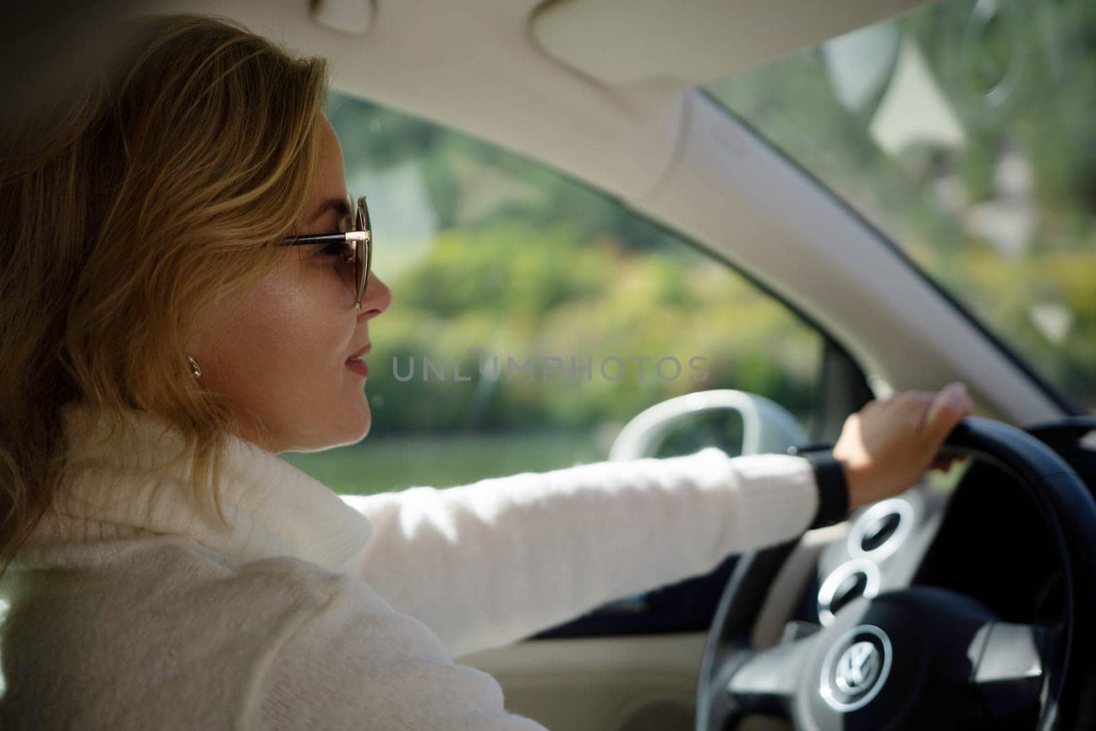 A blonde woman in a white sweater and jeans is driving. Happy woman sitting in the car