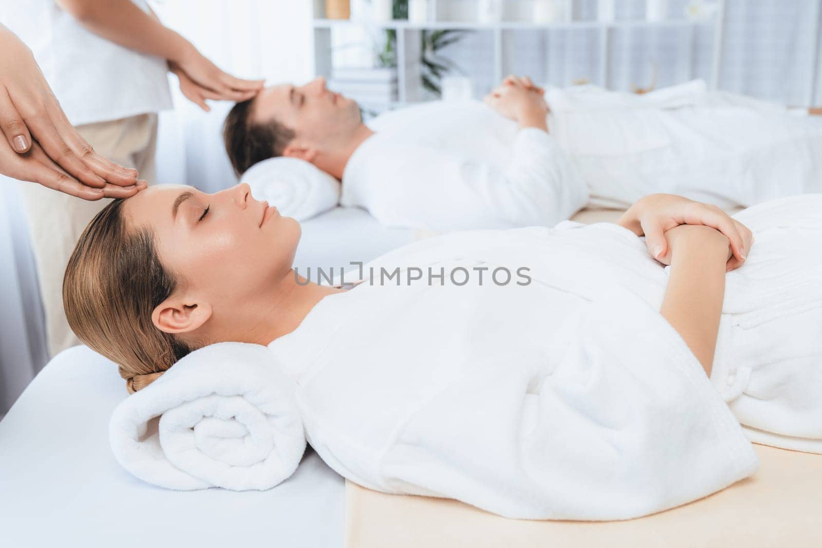 Caucasian couple enjoying relaxing anti-stress head massage and pampering facial beauty skin recreation leisure in dayspa modern light ambient at luxury resort or hotel spa salon. Quiescent