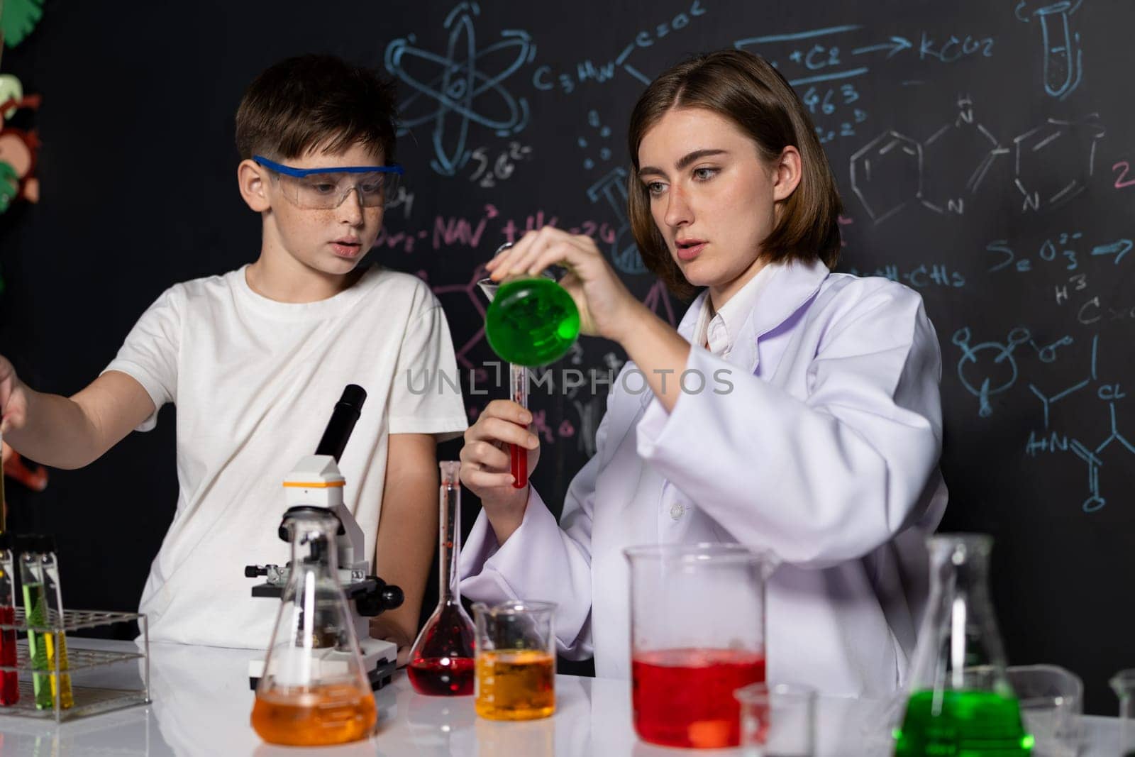 Teacher support schoolboy in laboratory. Schoolboy and teacher stand and experiment about science of chemistry in STEM class using liquid in glass container. Instructor mixing solution. Erudition.