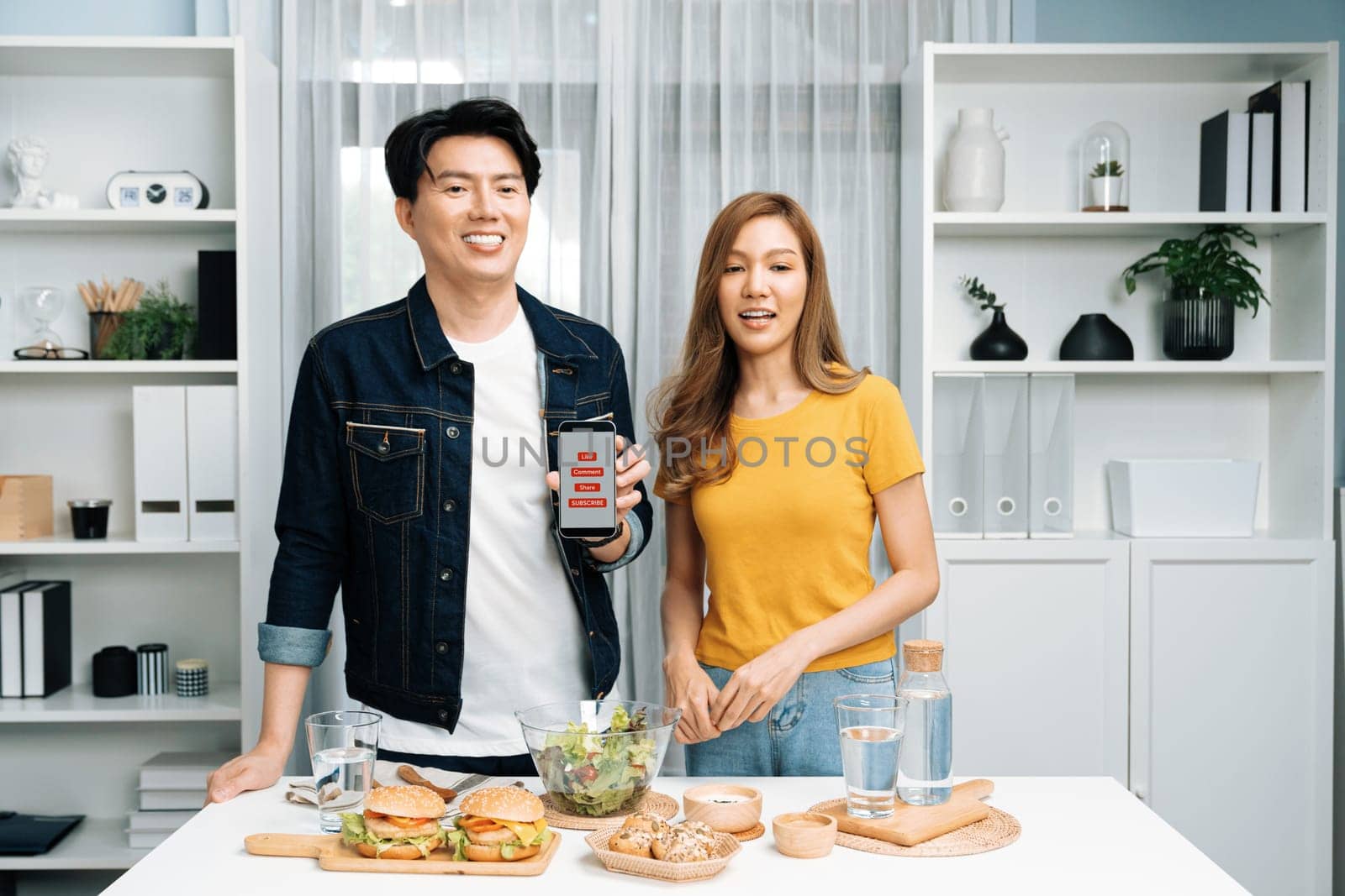 Chef influencers reading comment on phone for answering time on social media cooking show channel live streaming menu dish mixed salad, bun bread wholegrain and hamburger easy menu at home. Infobahn.