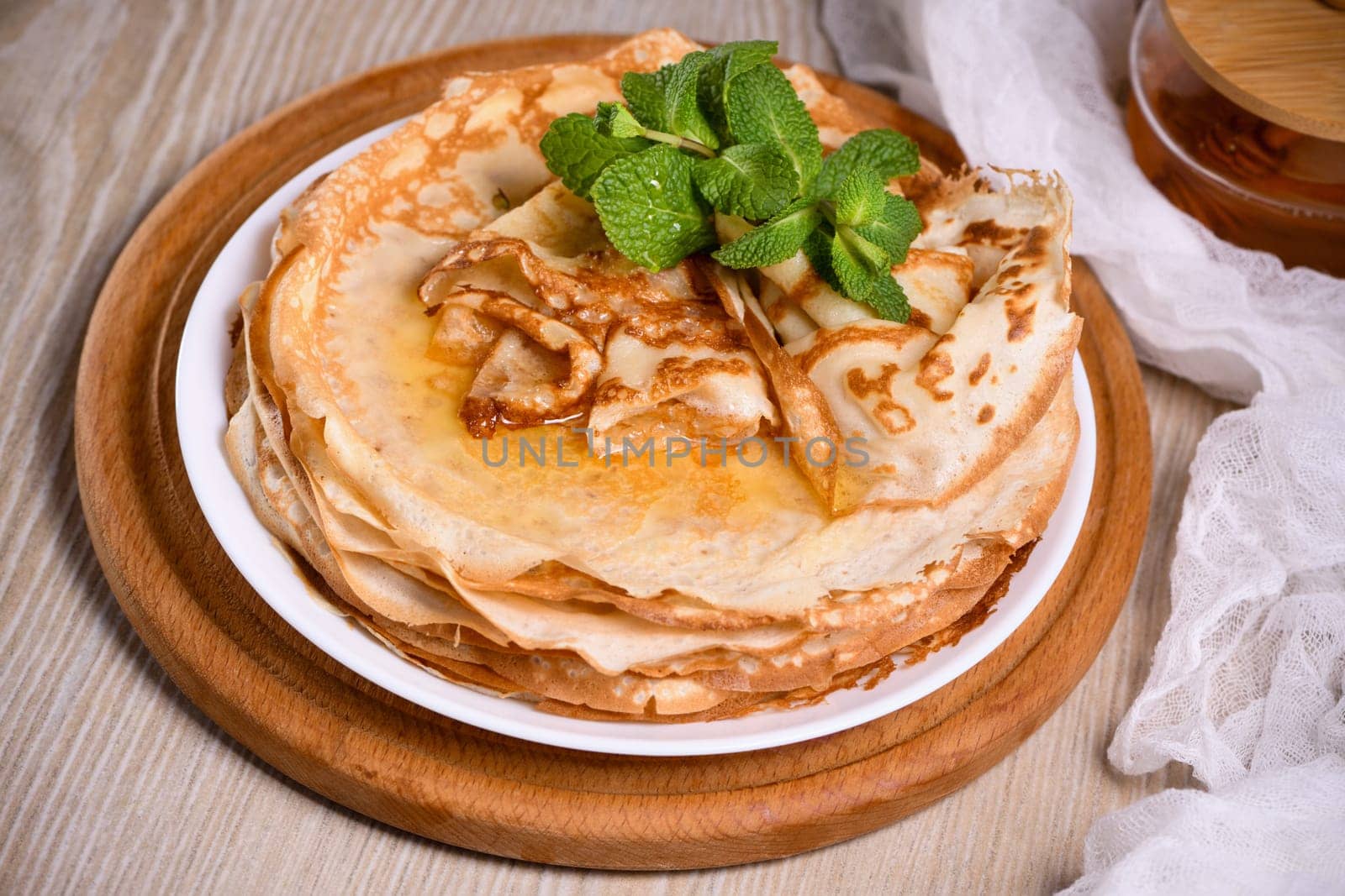 Homemade thin crepe (pancakes) with honey stacked in a stack, on a table with milk and eggs in a basket. Country style food. Traditional Slavonian, pagan holiday Maslenitsa