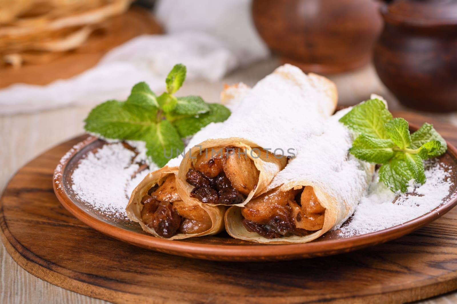 Homemade thin pancakes. The apples are cooked in a buttery caramel sauce with raisins and cinnamon and stuffed into a thin pancake. Garnish with powdered sugar and mint. Food in a rustic style.