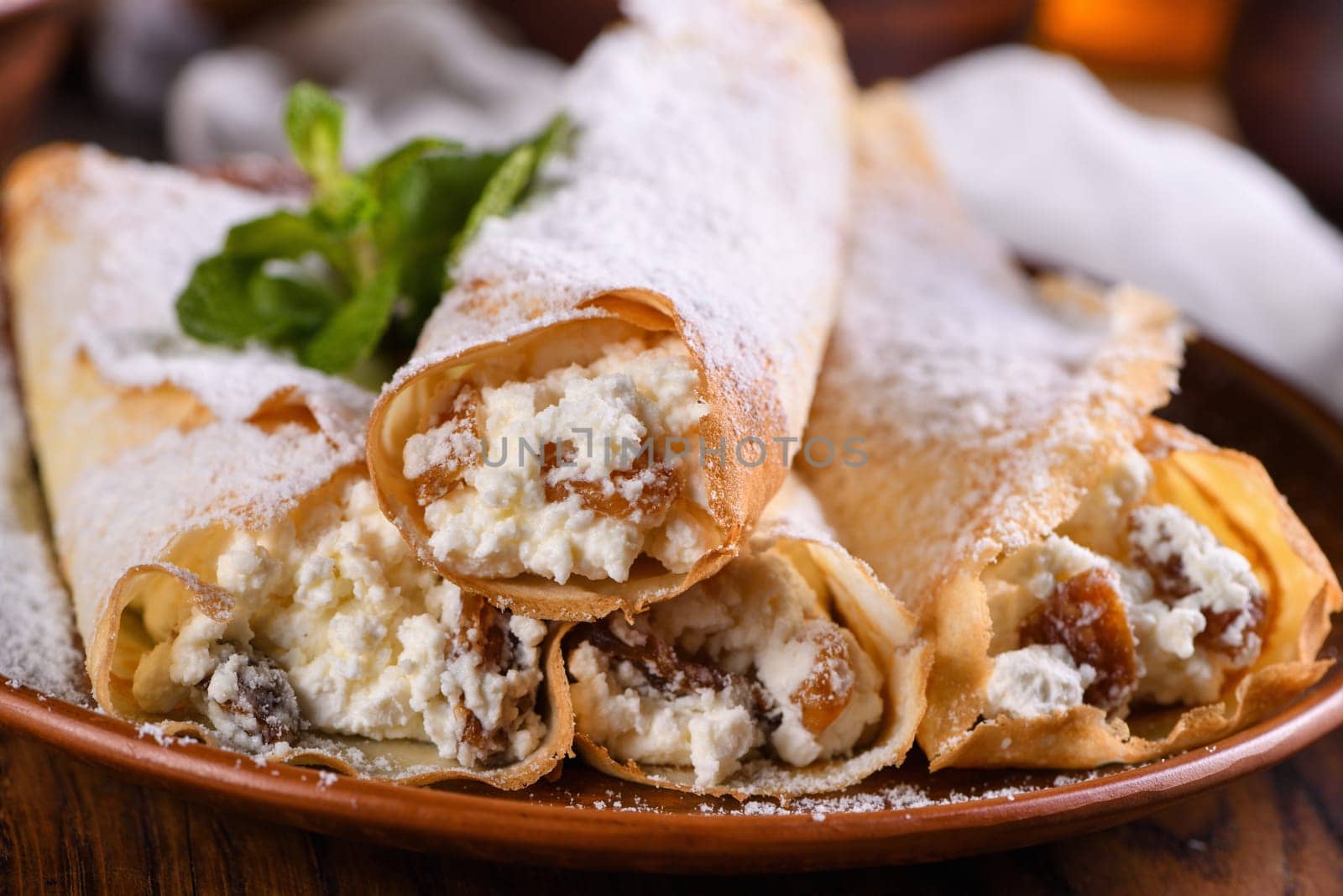 Thin pancakes filled with cottage cheese, honey and raisins, rolled in the form of a tube, sprinkled with powdered sugar, garnished with mint. Festive dish for the pagan Slavic holiday Maslenitsa