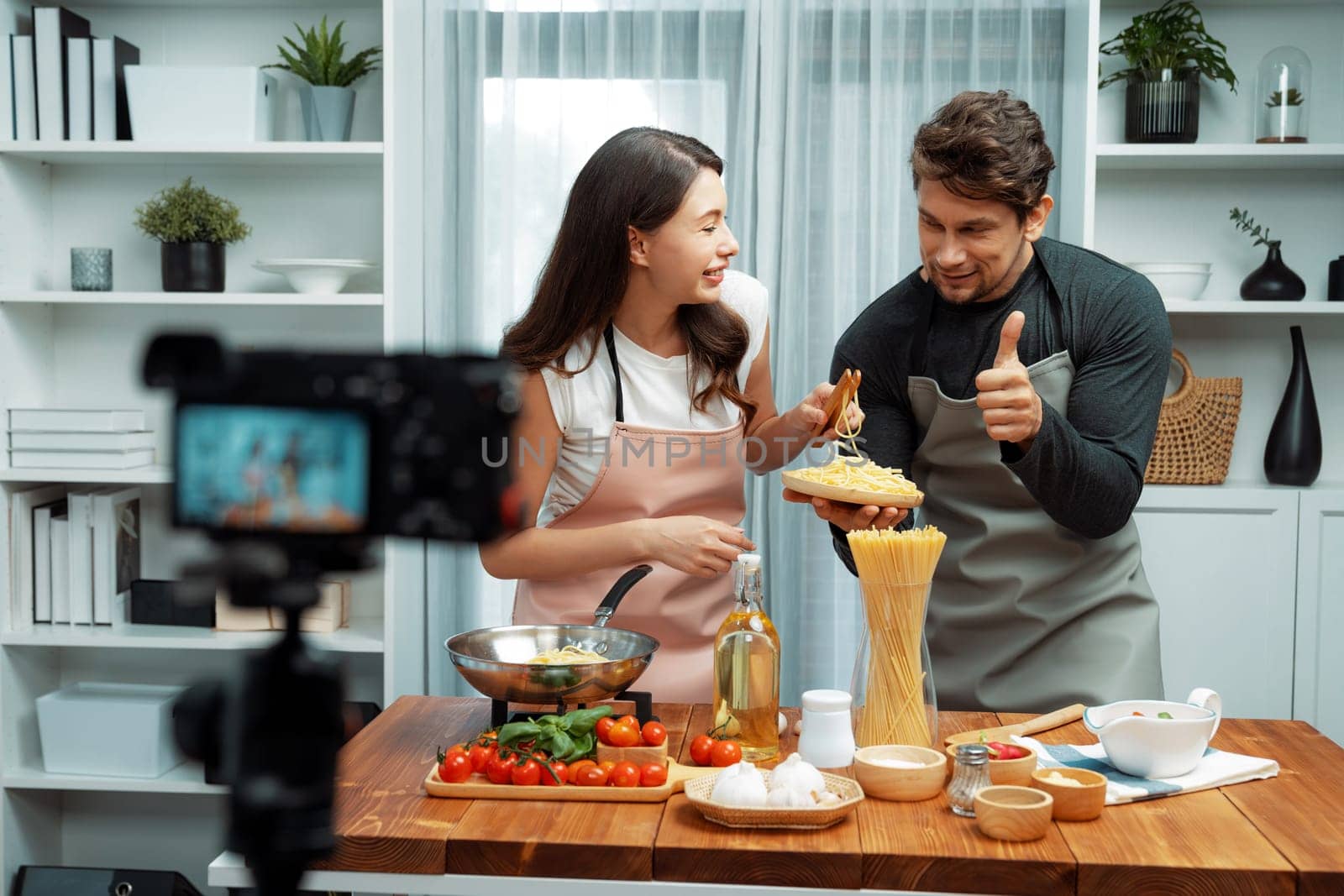 Couple chef influencers cooking special homemade of spaghetti with tongs taking to frying pan, putting seasoning and tasty sauce to make good flavor, recording on camera with live chanel. Postulate.