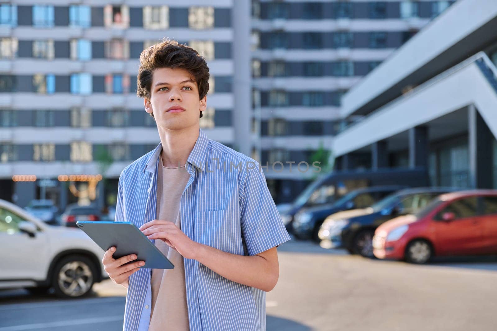 Young male using digital tablet on city street. Handsome guy student 19-20 years old, using pad for leisure, studying, working. Technology, youth, education, urban style concept