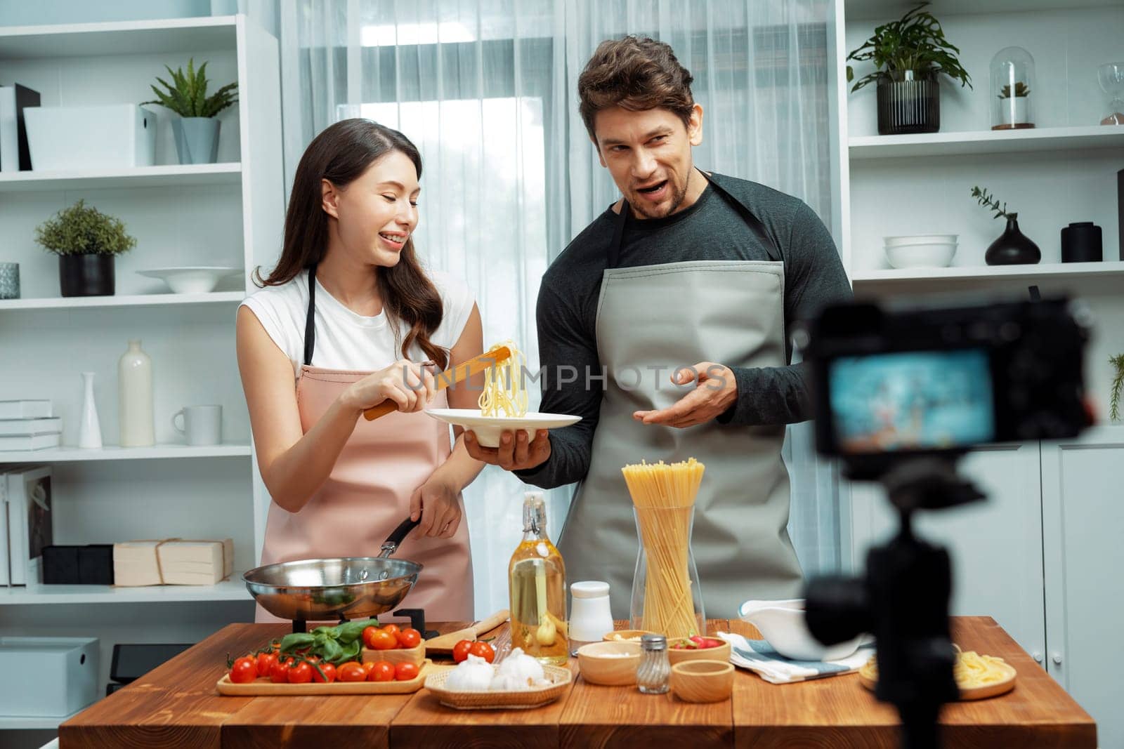 Couple chef influencers cooking special homemade of spaghetti with tongs taking to frying pan, putting seasoning and tasty sauce to make good flavor, recording on camera with live chanel. Postulate.