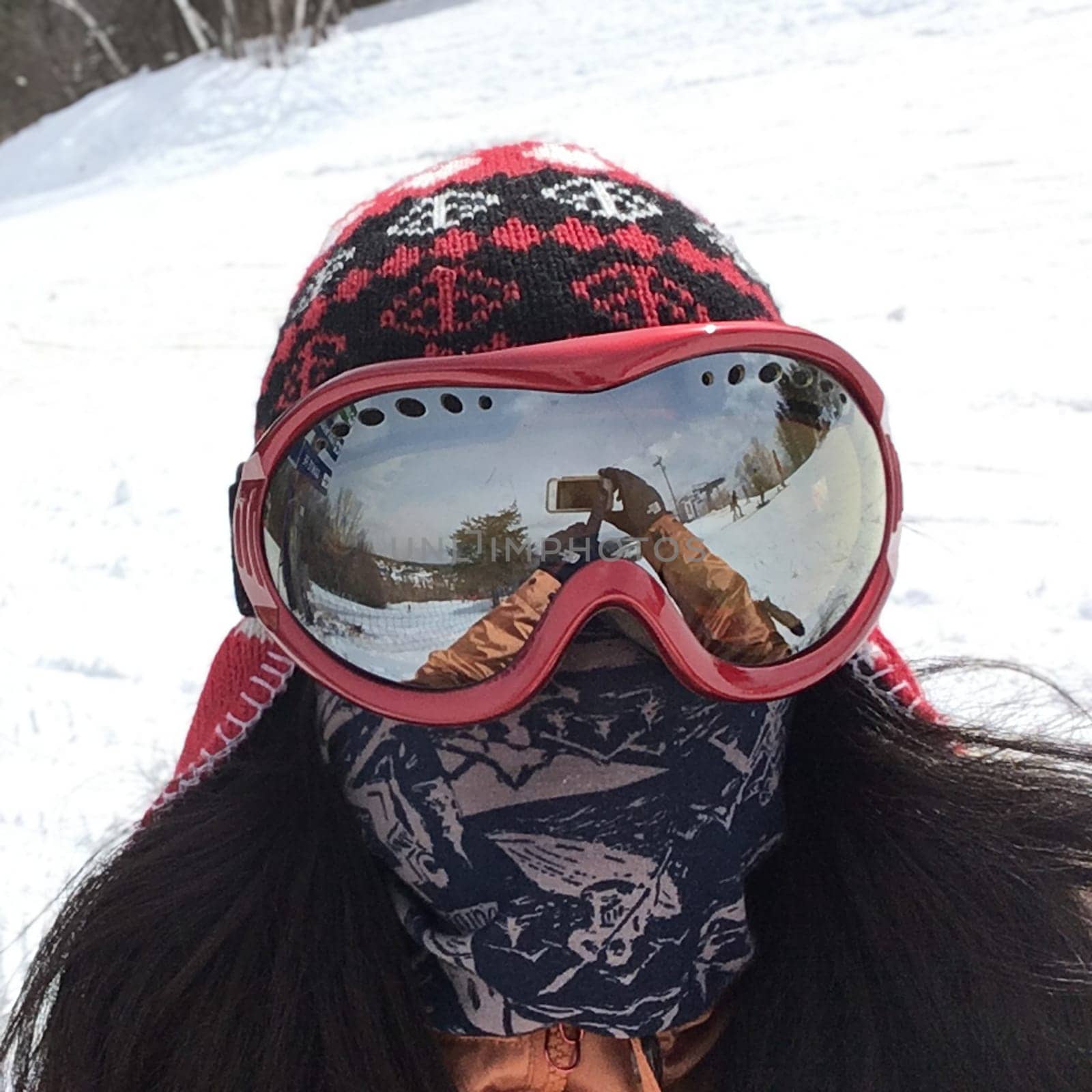 Person wearing ski goggles, a beanie, and a face covering, taking a selfie on a snowy day.