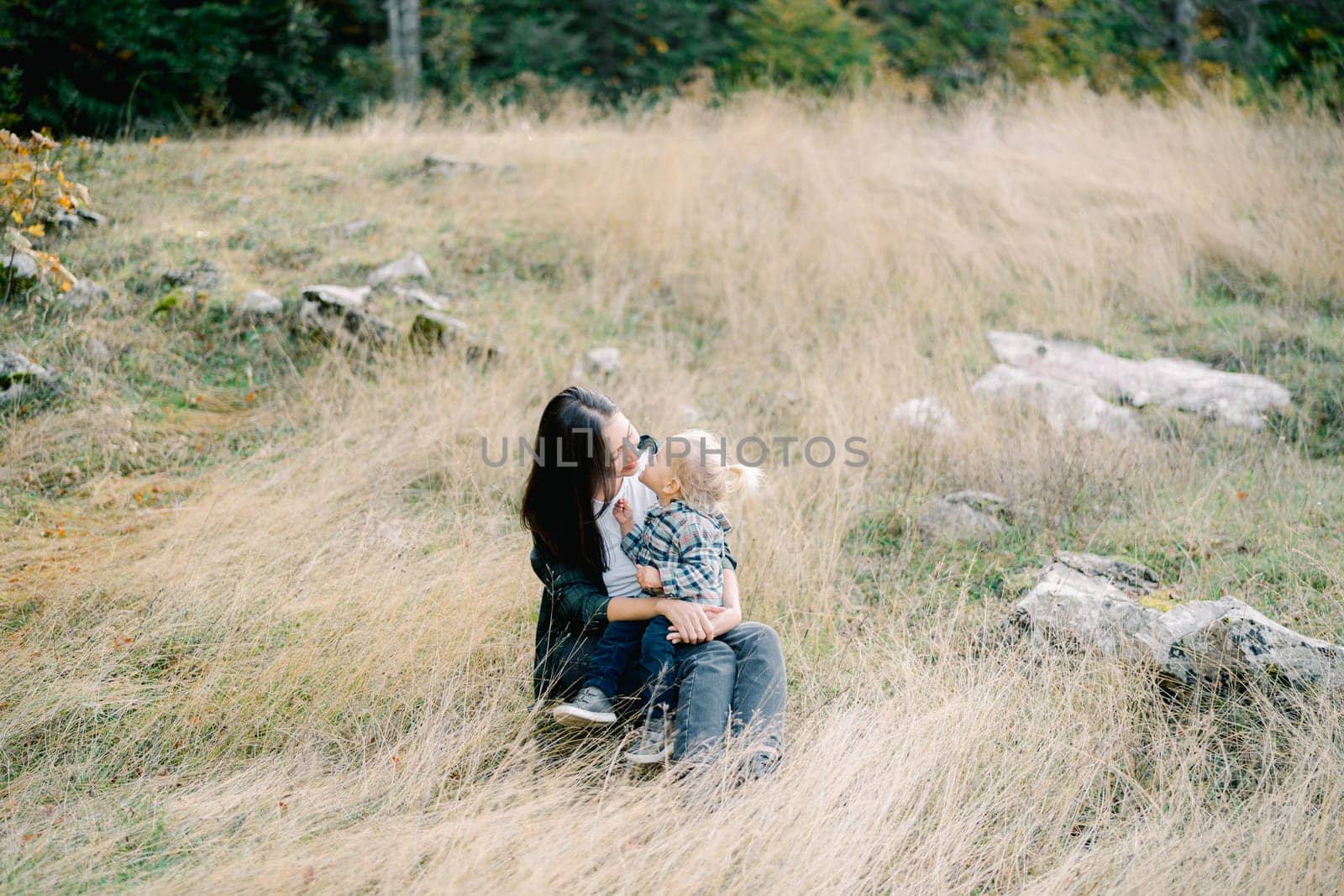 Smiling mom leaned towards a little girl sitting on her lap in a clearing in the forest. High quality photo