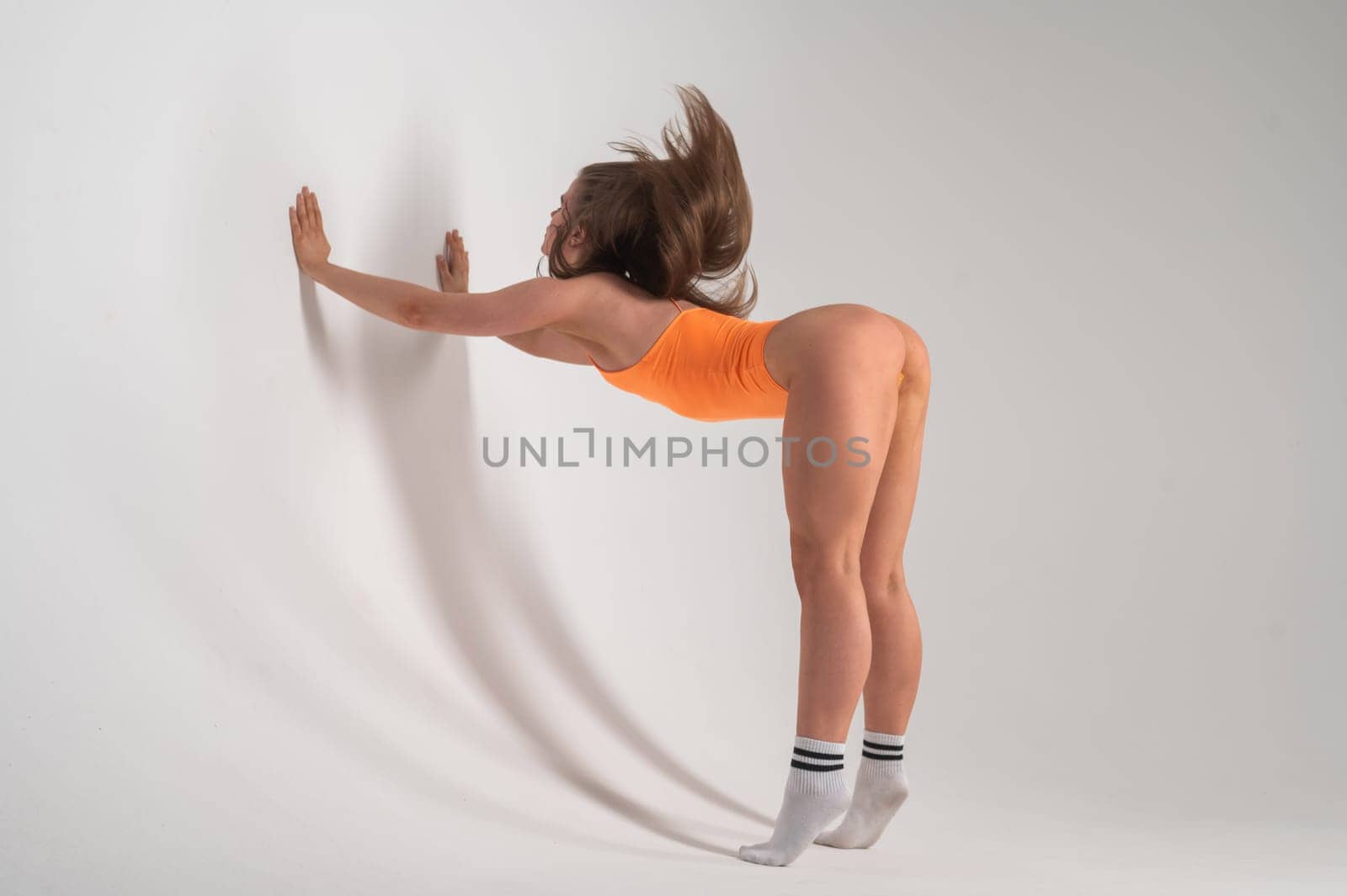 Caucasian woman in an orange bodysuit stretches her shoulders on a white background. by mrwed54
