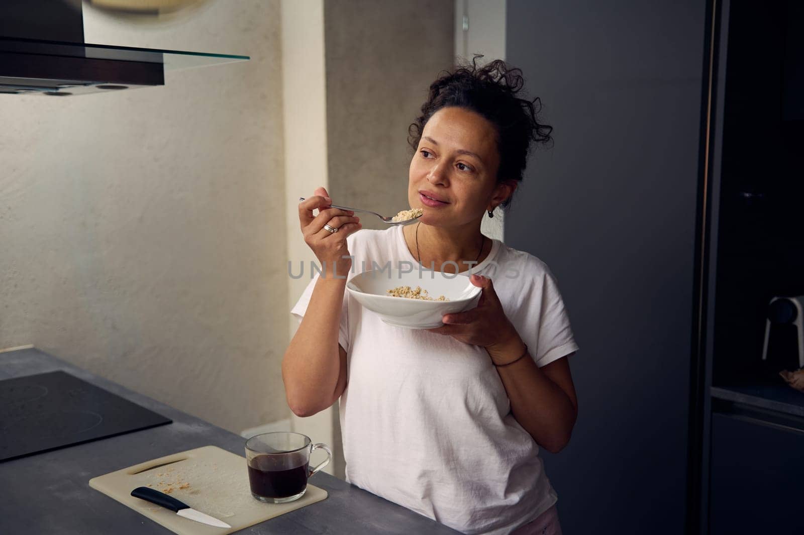 Young pretty woman in white t-shirt, eating a bowl of muesli at home. People. Food consumerism. Diet and slimming concept. Healthy lifestyle