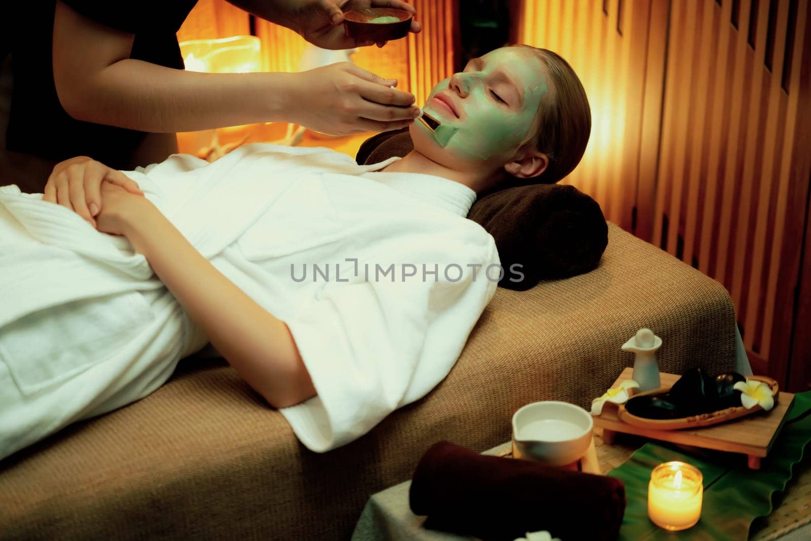 Serene ambiance of spa salon, woman customer indulges in rejuvenating with luxurious face cream massage with warm lighting candle. Facial skin treatment and beauty care concept. Quiescent