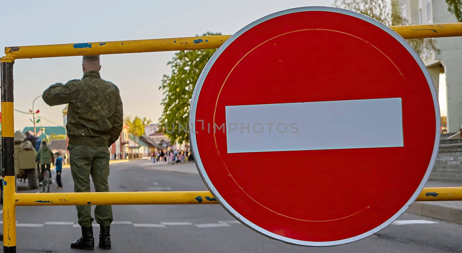 Armed soldiers at a roadblock with a no entry sign. Soldiers in full gear, carrying rifles. Roadblock made of metal barriers. No entry sign is large and red with a white border.