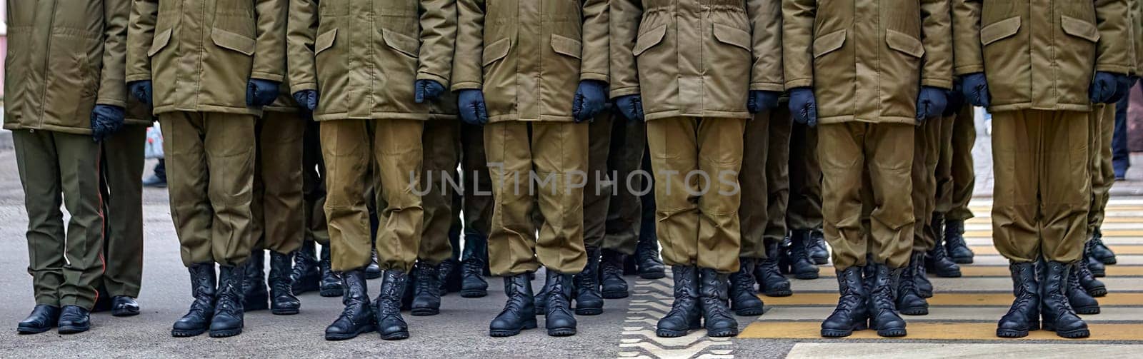 Army soldiers in uniform stand in formation on a concrete surface with yellow crosswalk lines. They wear combat fatigues and boots, showing discipline and readiness.