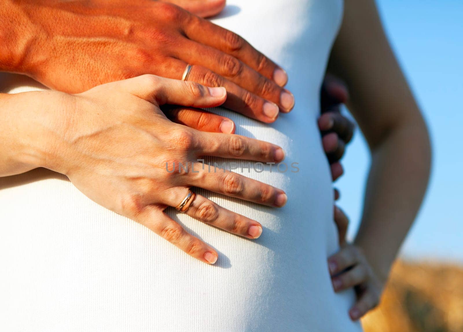 Pregnant belly being cradled by the hands of future parents. Maternity concept isolated on white background. Ideal for baby shower, pregnancy announcement, or Mothers Day celebration.